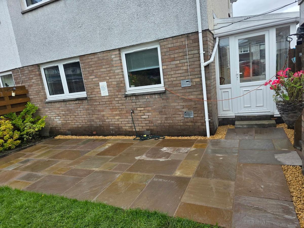 Sandstone patio outside a back porch with golden gravel edging and lawn